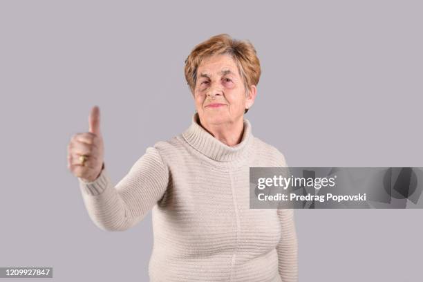 portrait of happy senior woman with thumbs up on studio background - happy woman thumbs studio stock-fotos und bilder