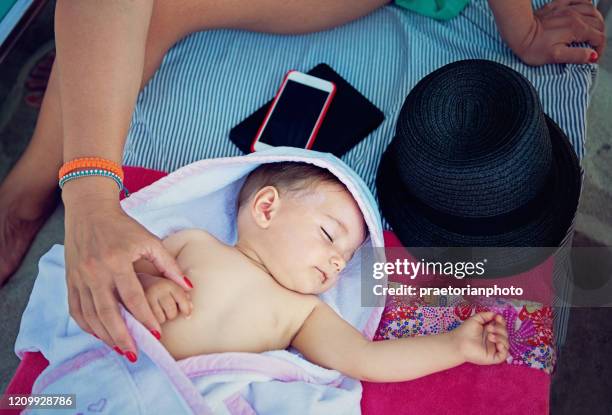 mother is stroking her sleeping baby under the beach umbrella - baby suncream stock pictures, royalty-free photos & images