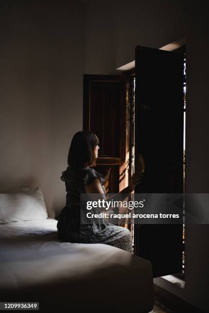 young woman sitting on a bed in front of window - bed sun stock pictures, royalty-free photos & images