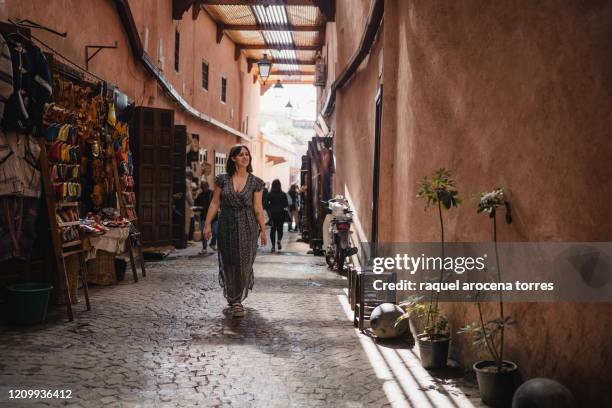 front view of young woman walking in the marrakech souk with a long dress - zoco fotografías e imágenes de stock