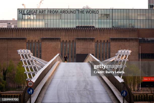 Walker crossing the Thames Millenium Bridge in front of Tate Modern during the lockdown at 7pm on 9th April 2020 in London, United Kingdom. Normally...