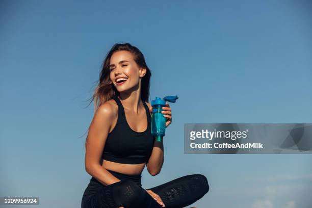 la donna fitness beve acqua di fronte allo sfondo del mare - struttura muscolare del torso foto e immagini stock