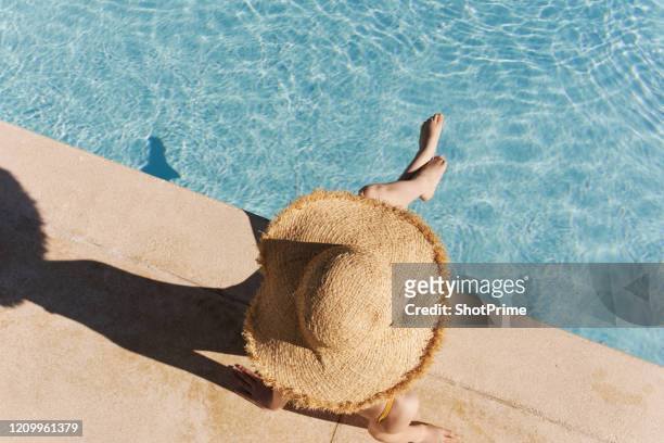 the girl in the big hat sits on the edge of the pool, the face is not visible - women tanning beach drink stock-fotos und bilder