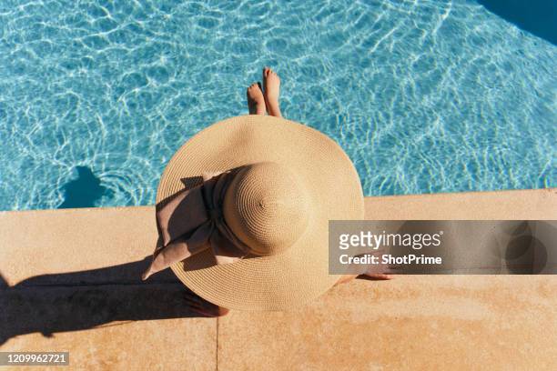 woman in hat lies near the pool, bright sun - hair spa foto e immagini stock