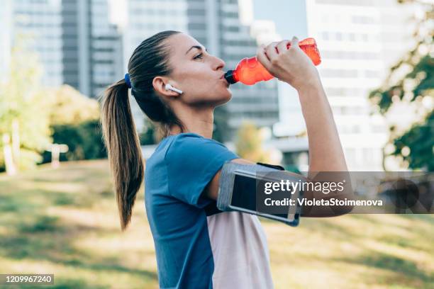 sportliche frau trinkwasser nach dem training - joggerin park stock-fotos und bilder
