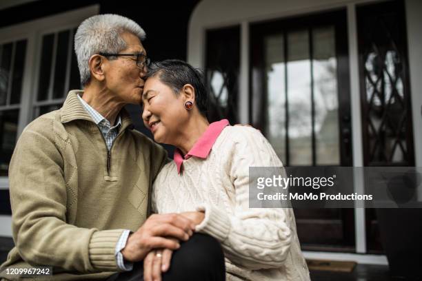 senior couple embracing in front of home - older asian couple stock-fotos und bilder