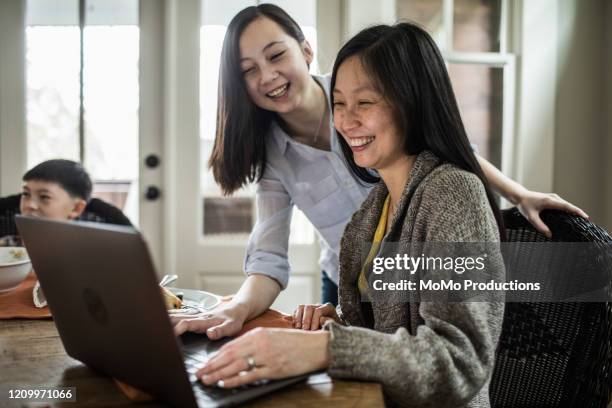 daughter helping mother with laptop at breakfast - asian girl doing online shopping ストックフォトと画像