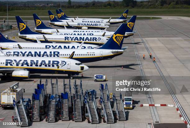 Three people walk on the runway amongst parked and temporarily out of service Ryanair passenger aircraft at Stansted Airport on April 15, 2020 in...