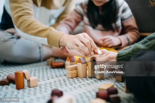 sluit omhoog van vrolijke aziatische ouders zitting op de vloer in de woonkamer die pret heeft en houten bouwstenen met dochter samen speelt - family together stockfoto's en -beelden