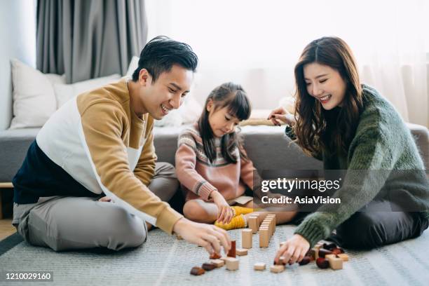 blije aziatische ouders die op de vloer in de woonkamer zitten die pret hebben en houten bouwstenen met dochter samen spelen - asian young family stockfoto's en -beelden