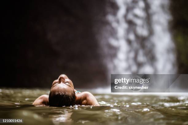 young carefree woman enjoying in water near the waterfall. - bali waterfall stock pictures, royalty-free photos & images