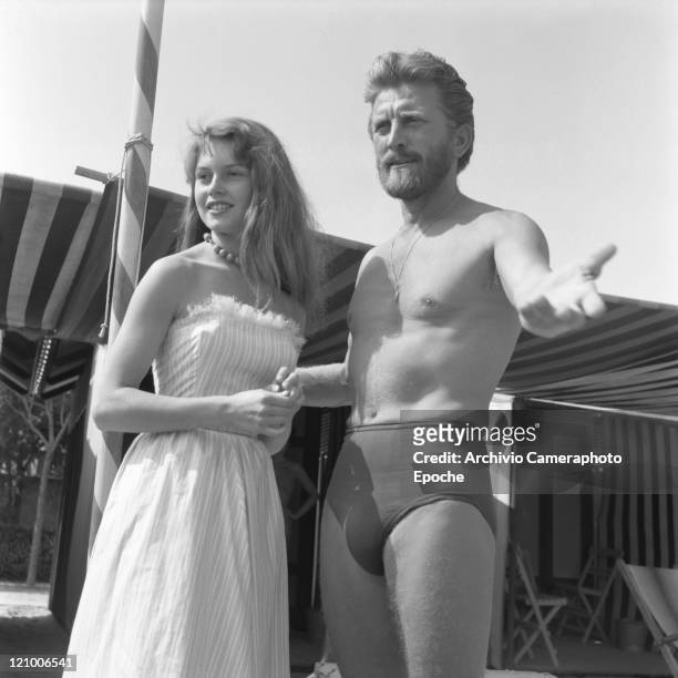 American actor Kirk Douglas, wearing a swiming suit and a necklace chainlet, portrayed with the actress Helene Portello on the Excelsior Hotel beach,...