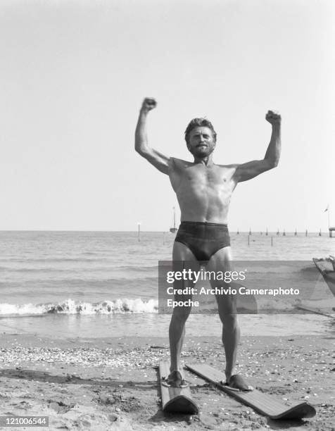 American actor Kirk Douglas, wearing a swimming suit and a necklace chainlet, portrayed while wearing a pair of waterski, on the Lido beach, Venice...