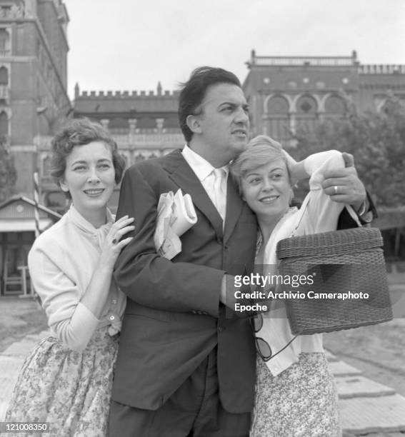Italian director Federico Fellini, wearing a suit and holding sunglasses, portrayed among the actress Valentina Cortese and his wife Giulietta Masina...