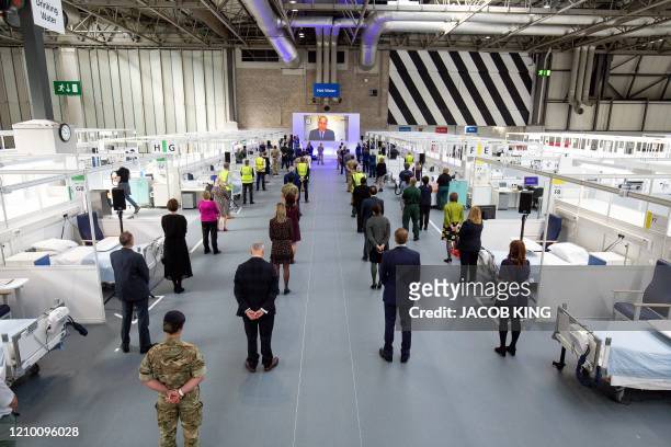 People observe social distancing measures as they stand amongst Hospital cubicles, as a giant screen displays an image of Britain's Prince William,...