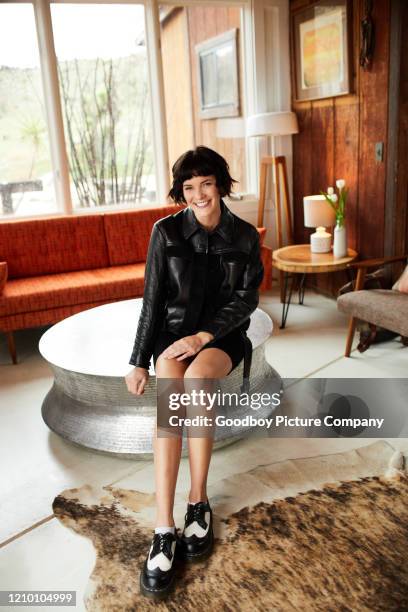 stylish young woman sitting on a table at home and smiling - leather skirt stock pictures, royalty-free photos & images