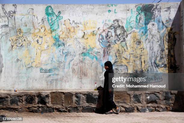 Yemeni girl walks by a graffiti create to illustrate the continuing war and calling for peace, on March 03 in Sana'a, Yemen. Yemen's continuing war...