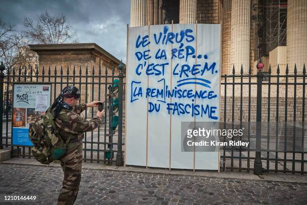 Protestor takes a photograph of graffiti at Place de la Madeleine which reads "the virus of the republic is the reminiscence of fascism" during...