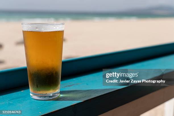beer glass on table by beach - lagerbier stock-fotos und bilder