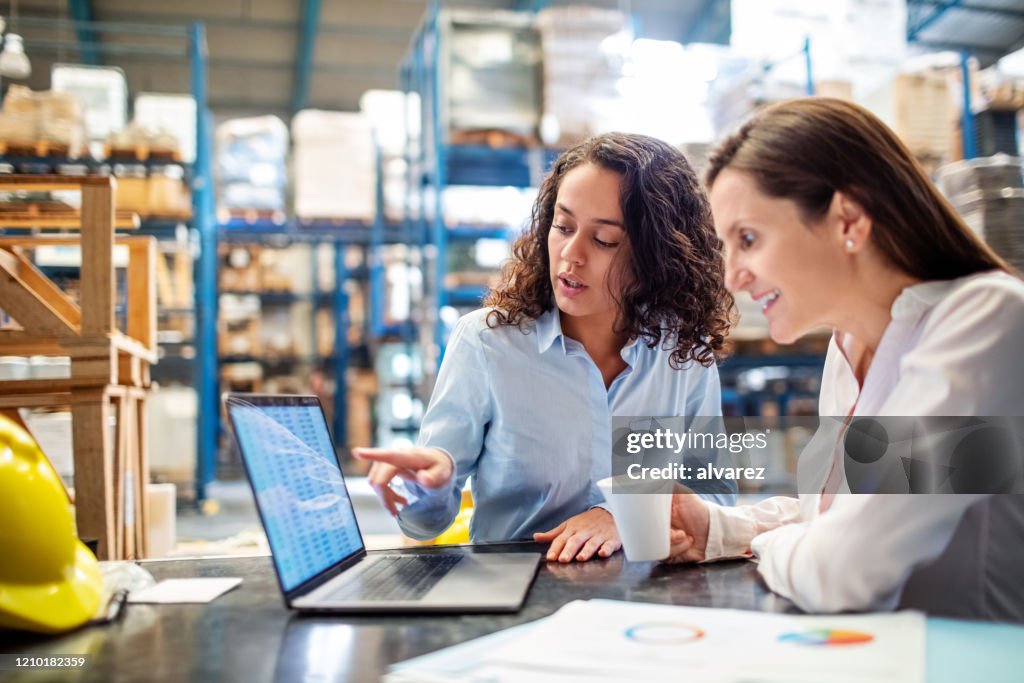 Woman showing inventory on laptop to warehouse manager
