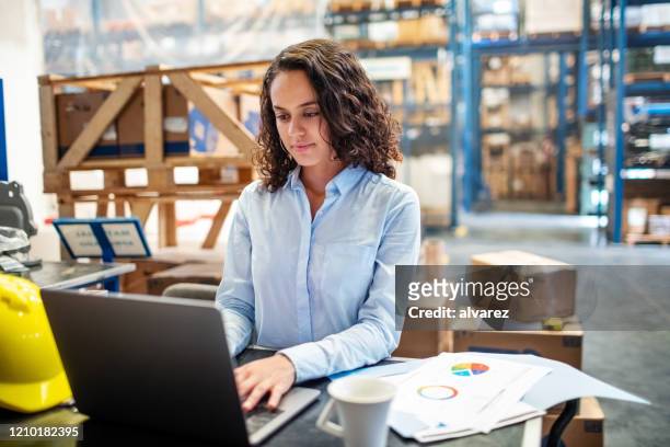 businesswoman updating stocks on laptop at warehouse - storage business stock pictures, royalty-free photos & images
