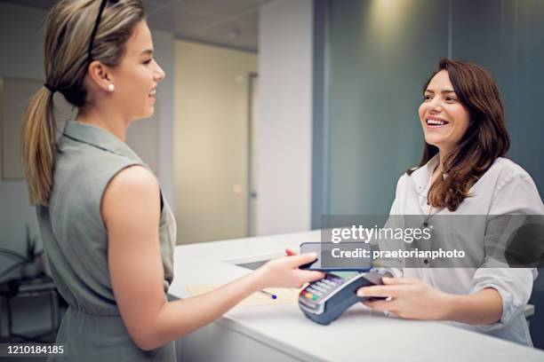 woman is paying on the reception desk in beauty treatment clinic using mobile phone - doctor phone stock pictures, royalty-free photos & images