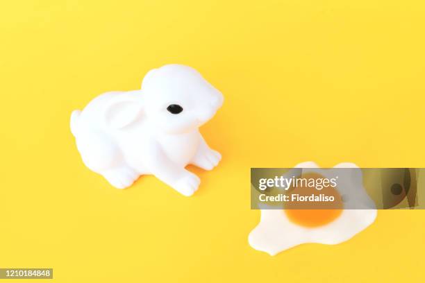 white toy neon rabbit with broken jelly egg candy on yellow background - broken easter egg stock pictures, royalty-free photos & images
