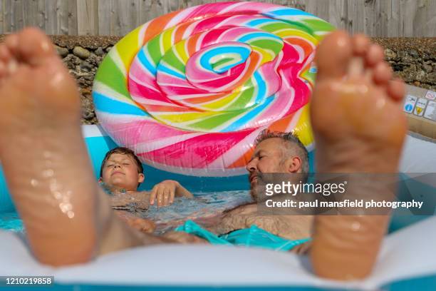 father and son messing about in paddling pool - lollipop man stockfoto's en -beelden