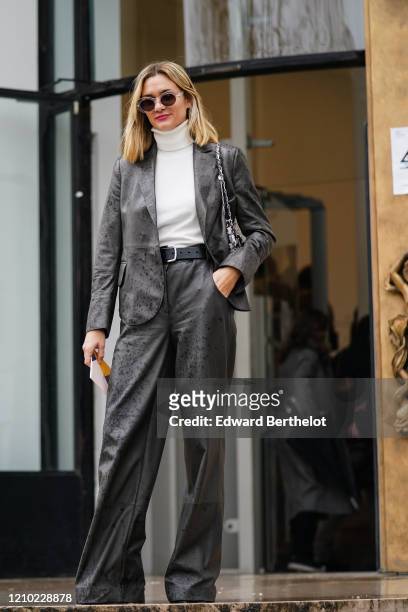 Anne-Laure Mais wears sunglasses, a white turtleneck, a grey leather jacket, a black belt, grey leather wide-legs full-length pants, a glittering...