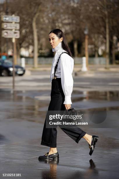 Yoyo Cao wearing Chanel white blouse, black pants with shoulder strap, black pants, patent shoes and mini Chanel bag outside the Chanel show during...