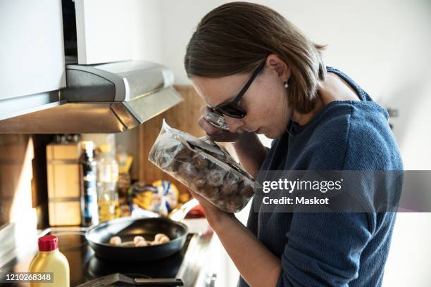 blind woman reading label on food packet through magnifying glass in kitchen at home - disabilitycollection stockfoto's en -beelden