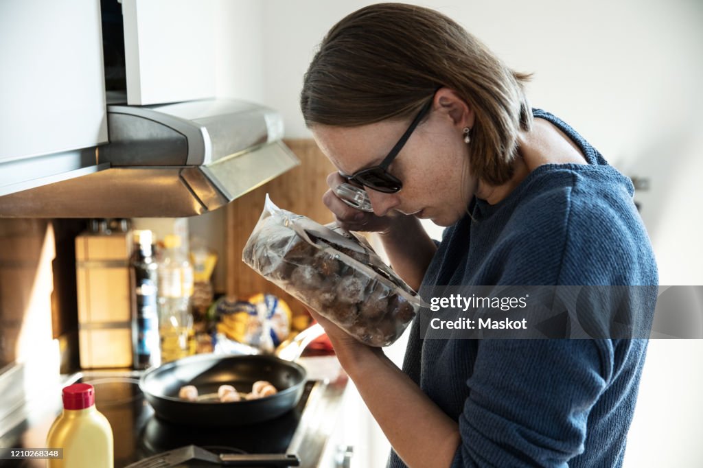 Blind woman reading label on food packet through magnifying glass in kitchen at home