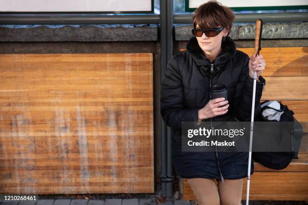 young blind woman with stick waiting at bus stop in city - blind woman stock pictures, royalty-free photos & images