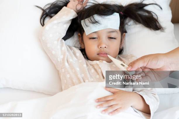 medical check up and treatment concept. mother is measure the temperature of little asian kid girl. sick child with fever and illness in bed. - krankheit stock-fotos und bilder
