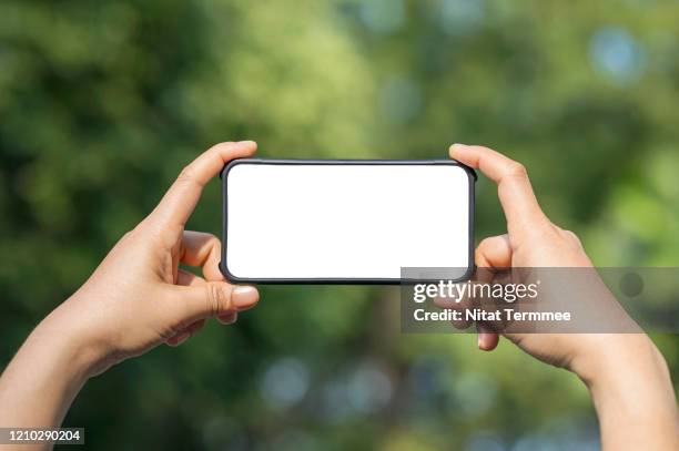 human hand hold smartphone on green blurred background. blank screen mobile phone for graphic display montage. - horizontal stock pictures, royalty-free photos & images