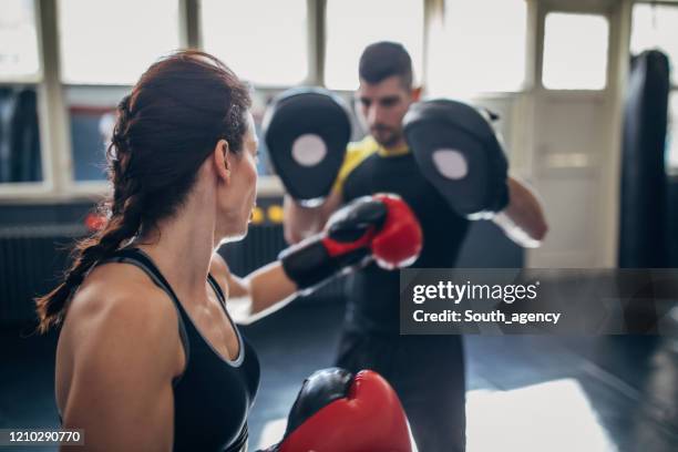 young woman on kick box practice, learning from her coach while sparring with him - kickboxing gloves stock pictures, royalty-free photos & images