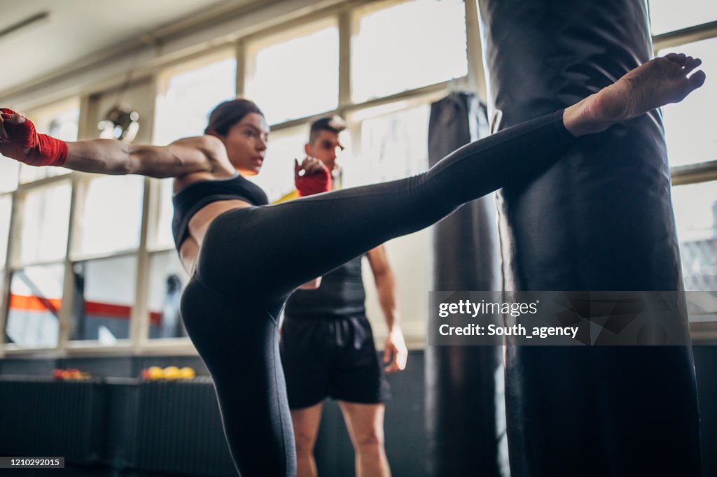 Istruttore di kick box che guarda come la donna kick boxer sta calciando punching bag sulla classe kick box