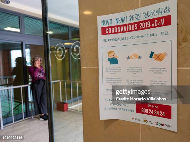 Woman is seen near a trilingual poster, in Portuguese, English and Chinese, with instructions on Coronavirus prevention hanging in the interior of...