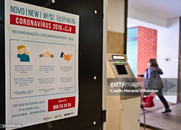 Woman is seen leaving the premises near a trilingual poster, in Portuguese, English and Chinese, with instructions on Coronavirus prevention hanging...