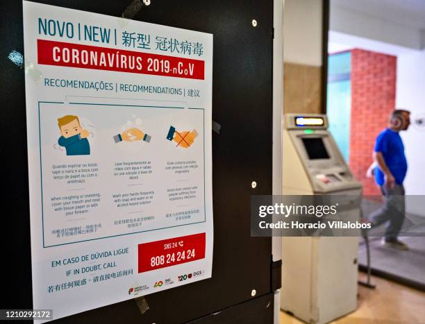 Man is seen walking into the premises near a trilingual poster, in Portuguese, English and Chinese, with instructions on Coronavirus prevention...