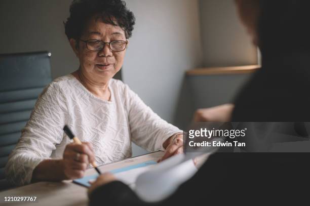 een aziatische chinese actieve hogere vrouw die bespreking met haar chinese agent over haar pensioeninvesteringsplan heeft dat wettelijk document ondertekent - woman filling out paperwork stockfoto's en -beelden