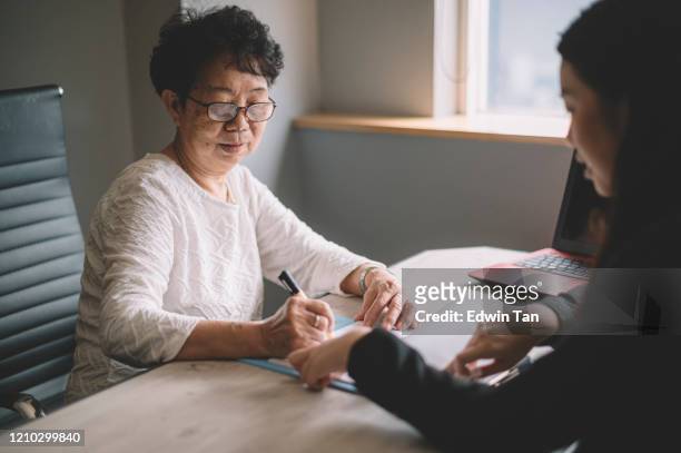 an asian chinese active senior woman having discussion with her chinese agent about her retirement investment plan signing legal document - two bank managers talking stock pictures, royalty-free photos & images