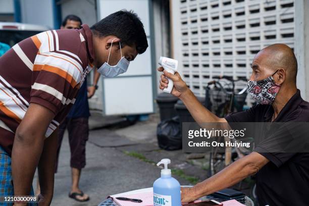 Migrant worker wearing protective face mask has his temperature checked by a security guard before leaving a factory-converted dormitory on April 17,...