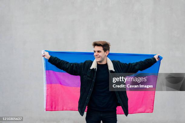 young man with the bisexual flag on a grey background - gay flag stockfoto's en -beelden