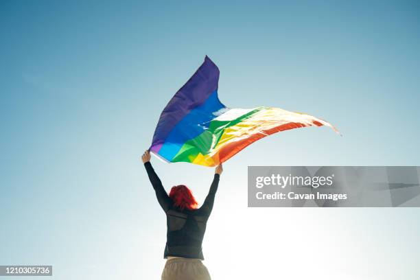 woman holding the gay rainbow flag on blue sky background. happiness, freedom and love concept for same sex couples. - transgender bildbanksfoton och bilder