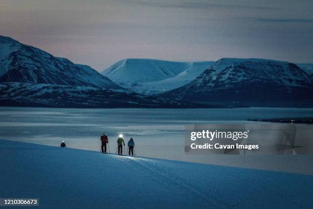 a group of 3 people skis at sunrise with ocean and mountains behind - night skiing stock pictures, royalty-free photos & images