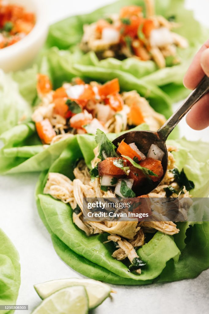 Adding pico de gallo to chicken lettuce tacos with a spoon