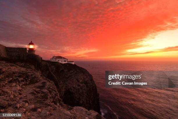 coastline landscape at sunset with reddish sky and a lighthouse lit on the cape of san vicente, portugal - headland stock-fotos und bilder