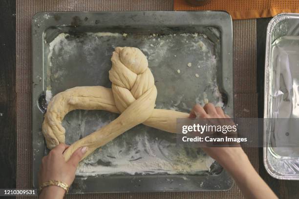 cropped image of hands braiding dough for challah bread in tray at table - challah stock pictures, royalty-free photos & images