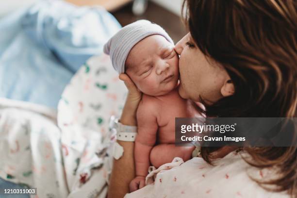 close up detail of mother kissing newborn son's cheek in hospital - born stockfoto's en -beelden
